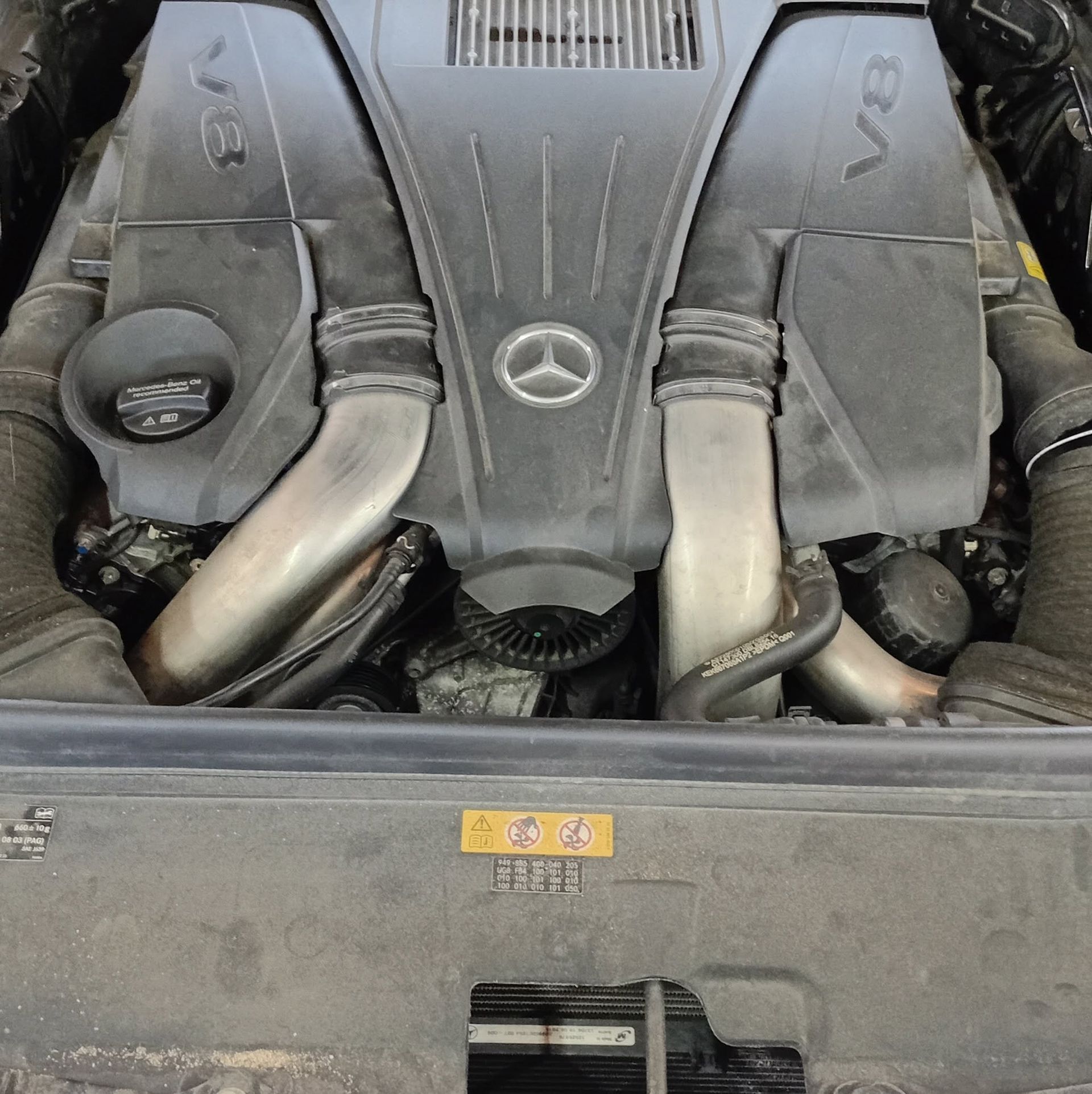 Mercedes engine bay with dual silver intake pipes and a central logo cover, viewed from above