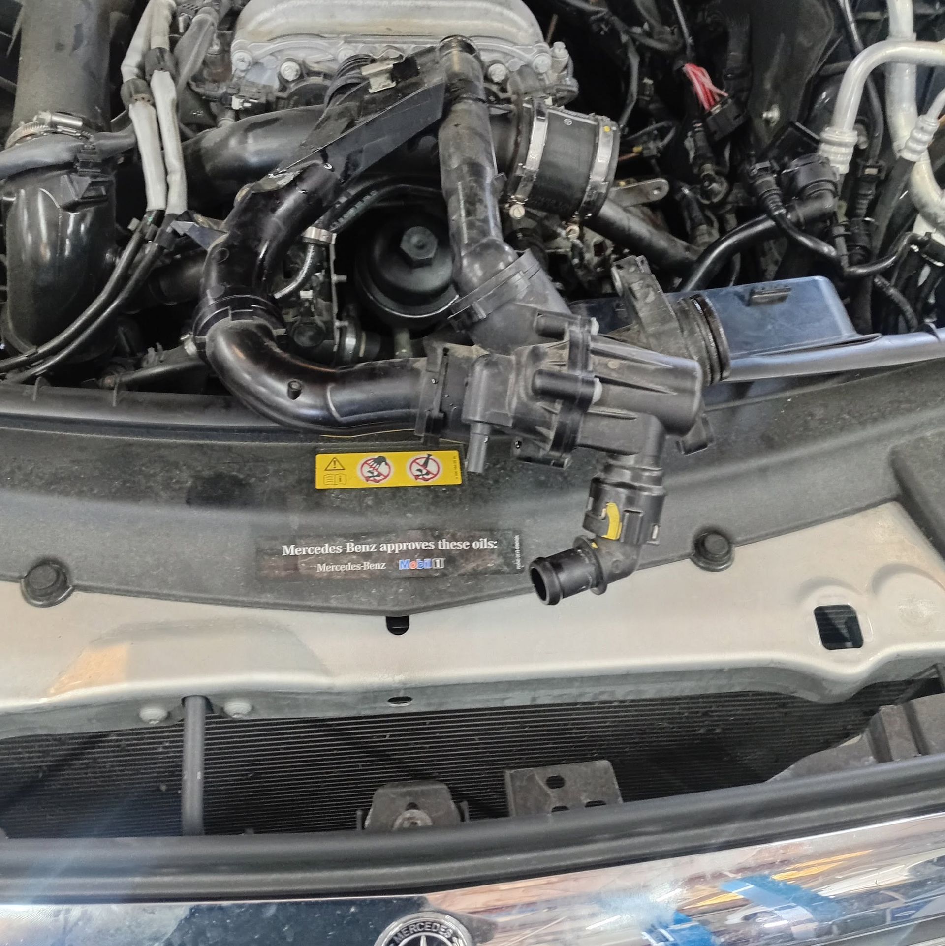 Open car hood showing a damaged engine bay with hoses, wiring, and front grille visible