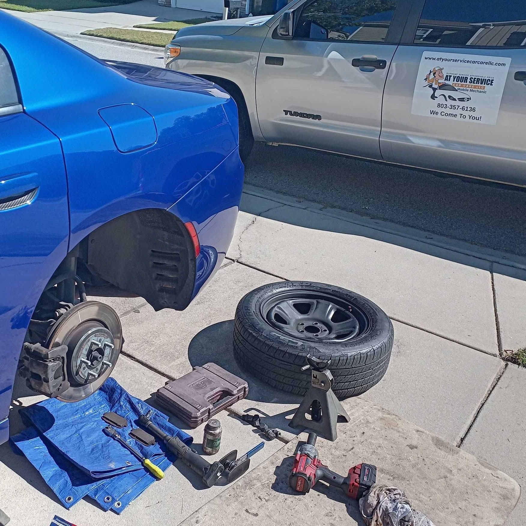 Blue car with rear wheel removed, tire on jack stands, and tools on the driveway beside it