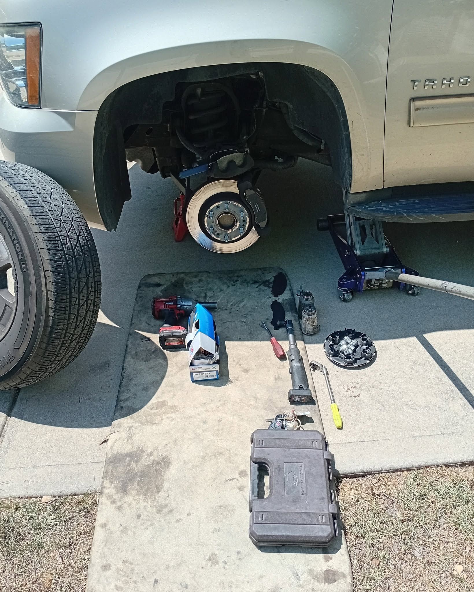 Car wheel removed, exposing brake rotor; tools and parts laid out on driveway during repair.