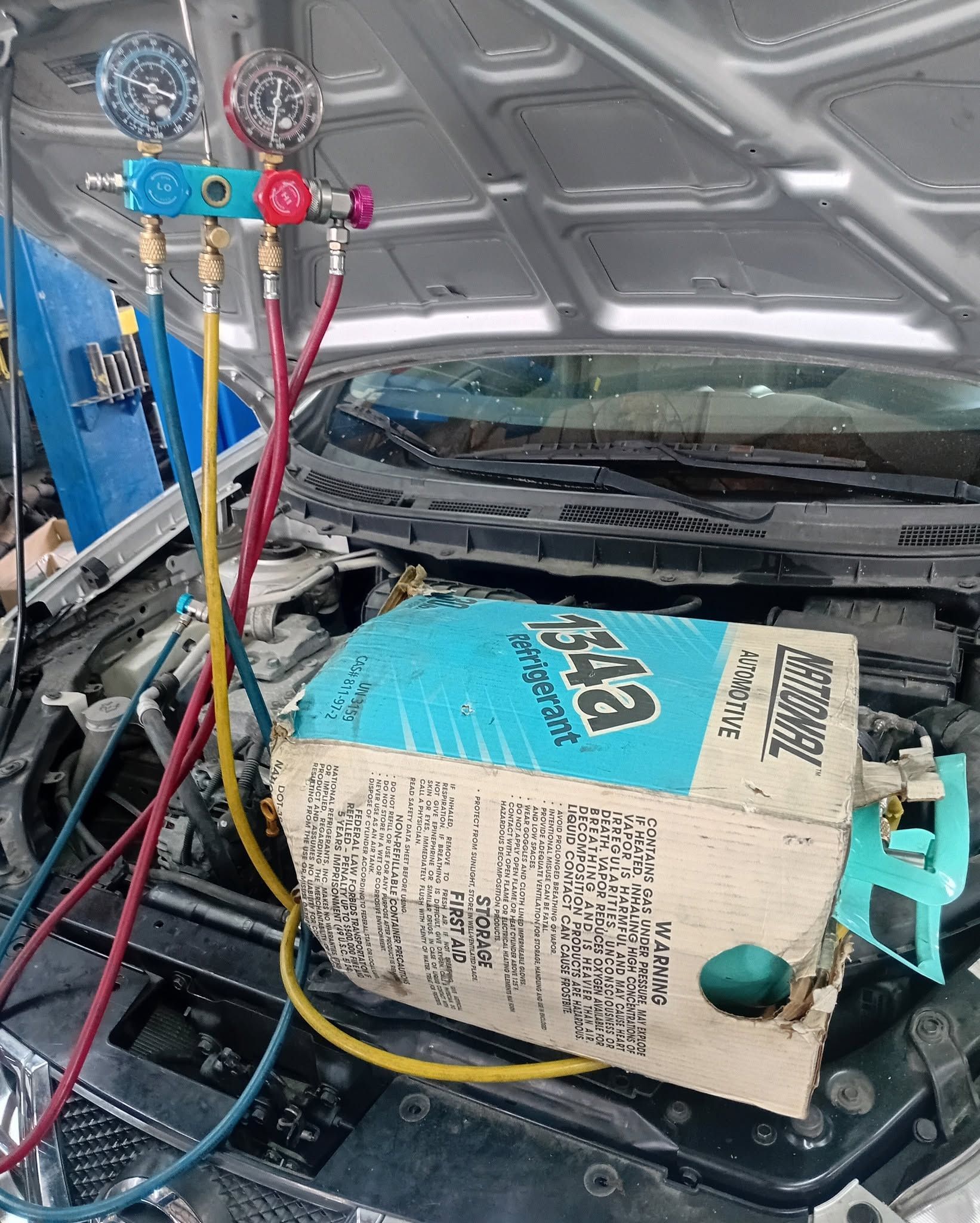 Car engine bay being serviced with colorful AC manifold gauges and hoses attached to the open hood