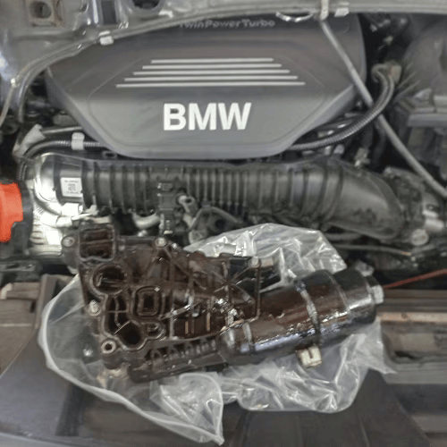 BMW engine bay with a black plastic intake part wrapped in clear plastic in the foreground