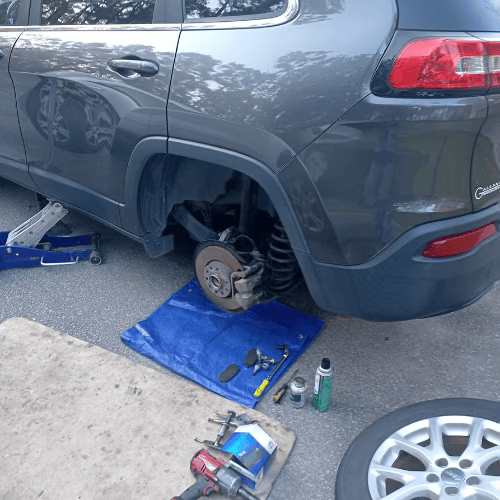 SUV with rear wheel removed, brake exposed, and tools on a blue mat during tire repair