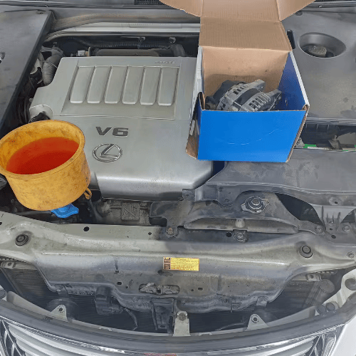 Car engine bay with a V8 cover, orange cup, and open box of parts resting on top
