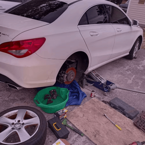 White sedan on jack with rear wheel removed, tools scattered on the ground during tire repair