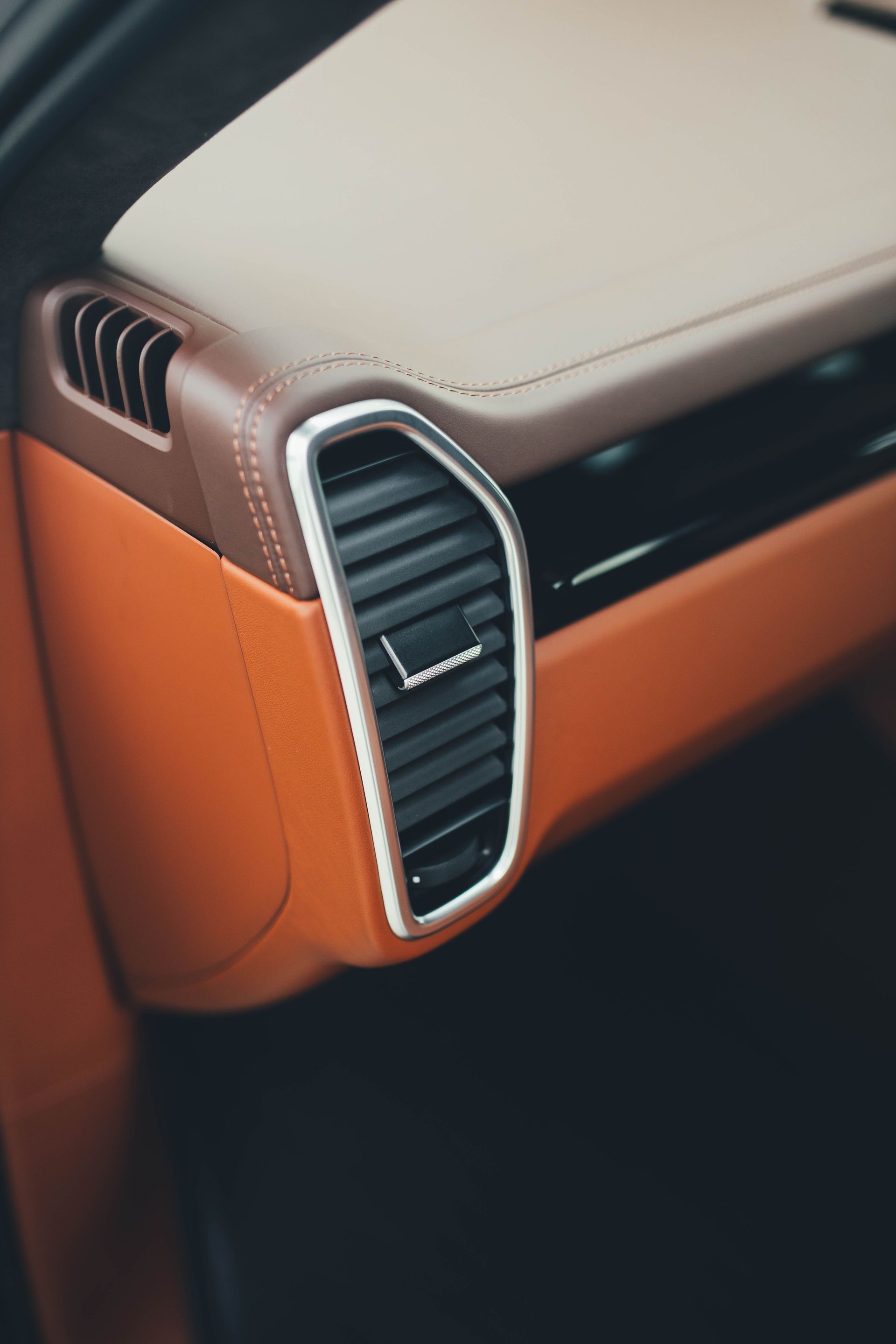 Close-up of a car dashboard air vent with black slats, silver trim, and orange interior panel