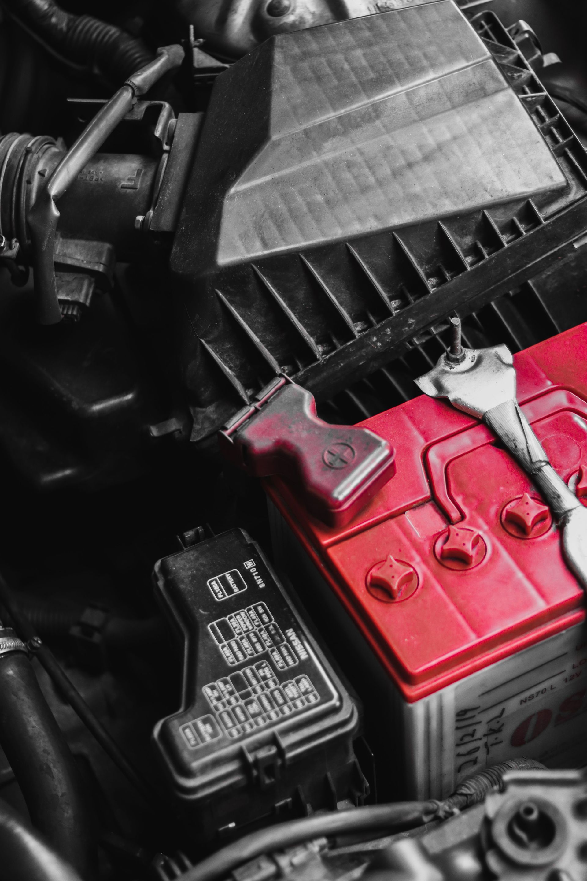 Close-up of a car engine bay with a red battery and black air filter box