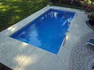 Backyard swimming pool with blue water, white deck, and stone patio