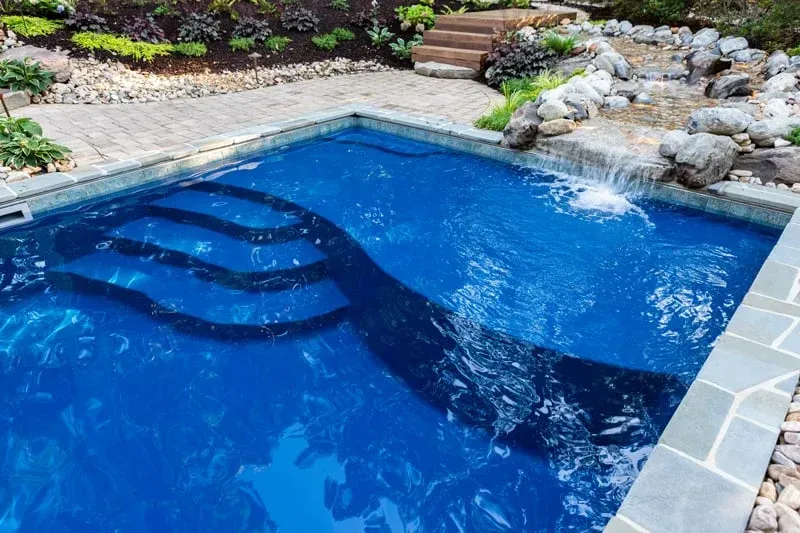 Blue backyard swimming pool with steps and stone edging, set beside a landscaped rock garden