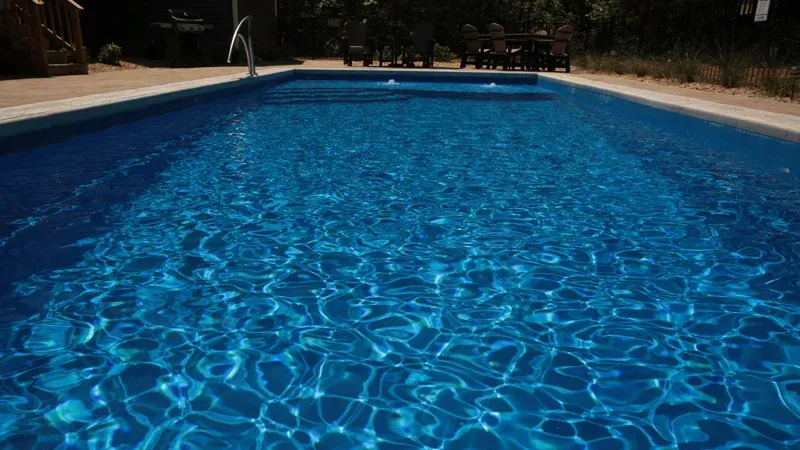 Blue swimming pool with rippling water and surrounding deck in bright sunlight