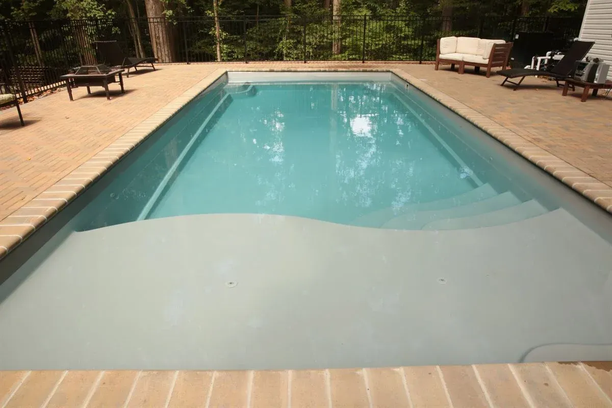 Outdoor swimming pool with turquoise water, tan deck, and trees in the background