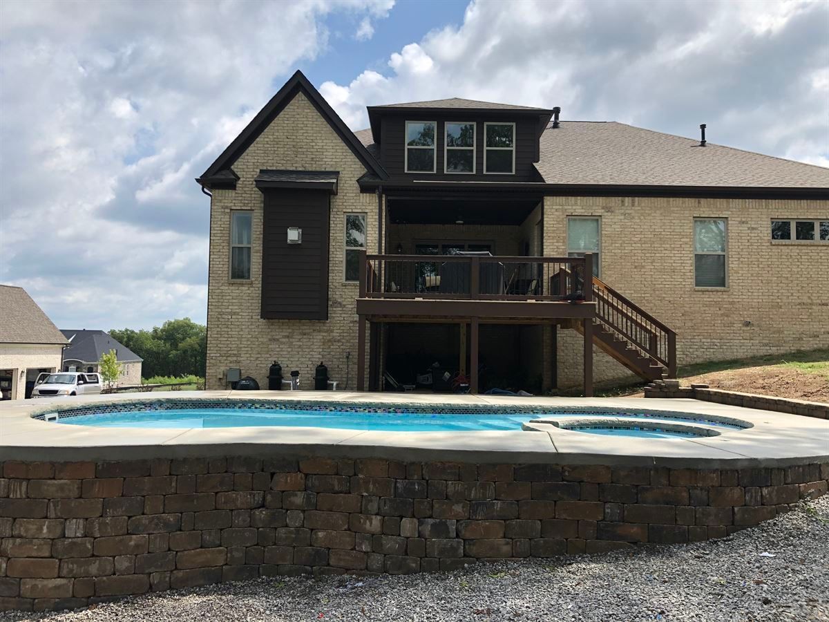 Backyard pool with stone retaining wall and a two-story house in the background