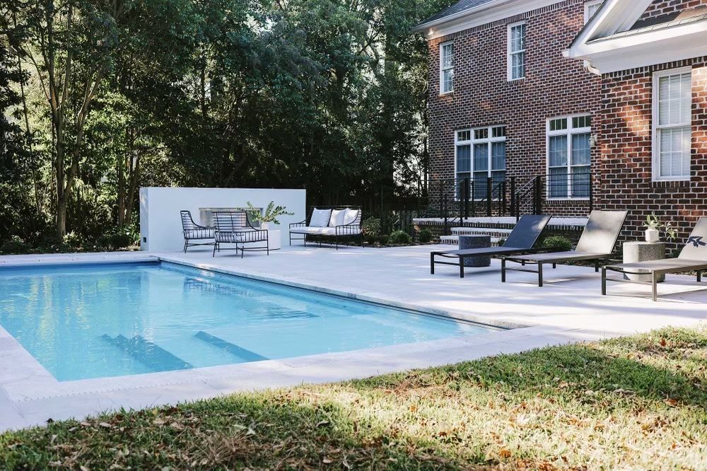Backyard pool beside a brick house with lounge chairs and a patio