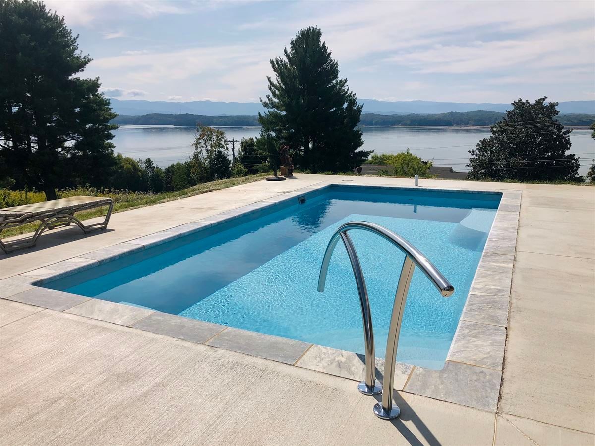 Concrete pool deck with a blue swimming pool, metal handrail, and a lake view in the background