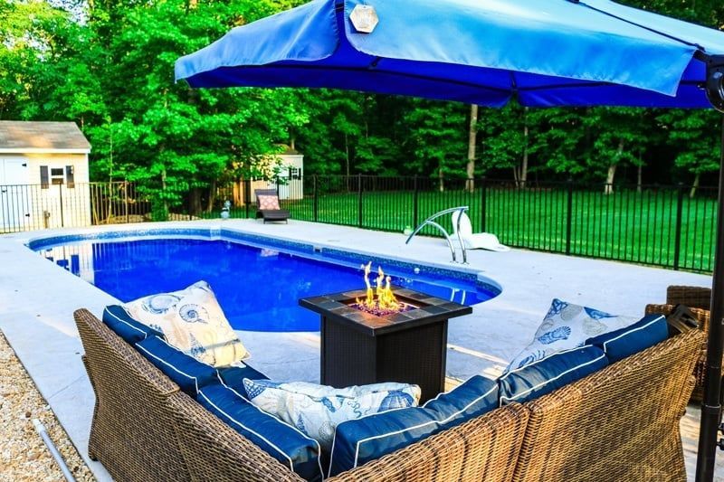 Backyard poolside patio with wicker seating, blue umbrella, and fire table beside a swimming pool