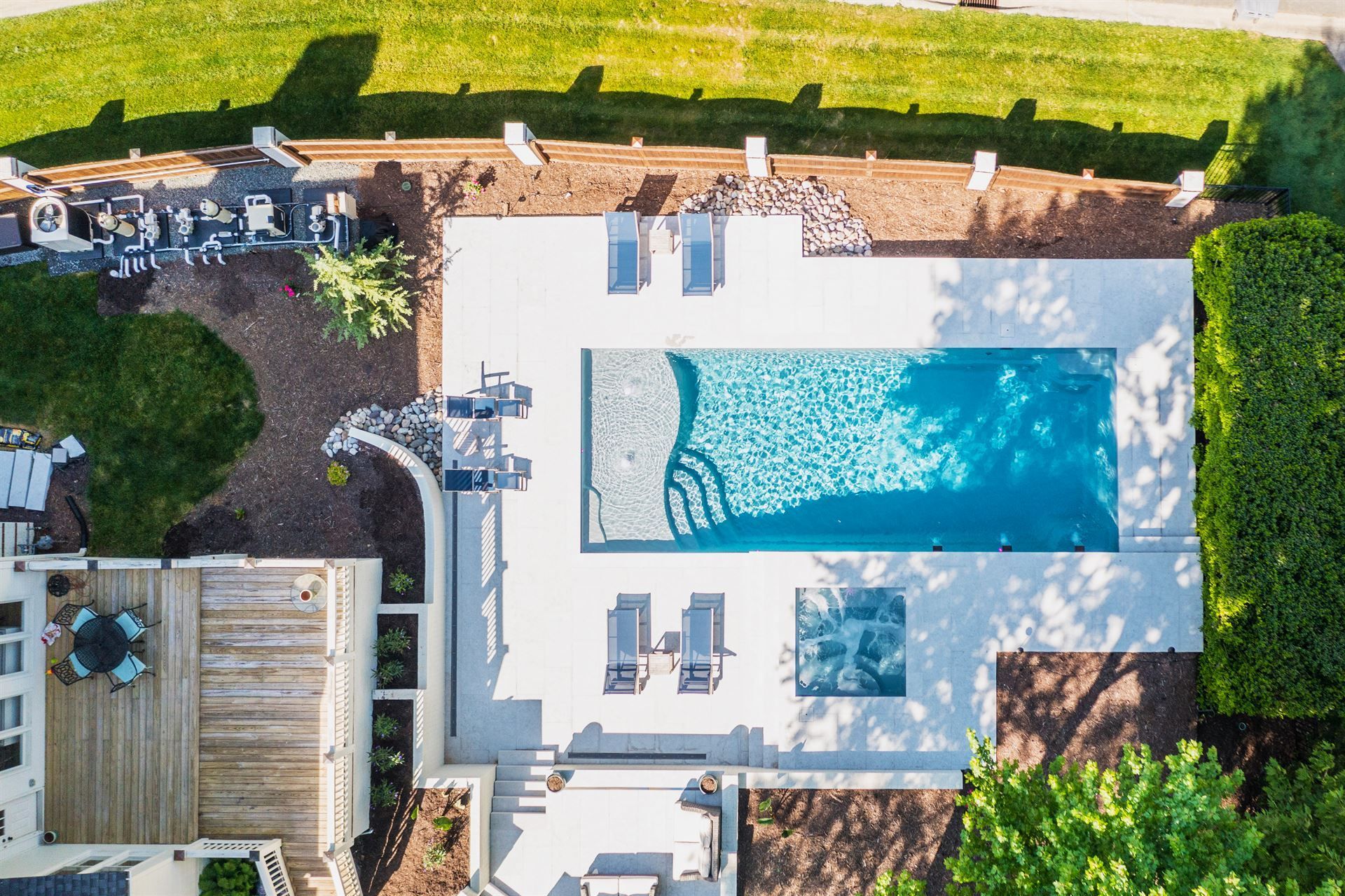 Aerial view of a backyard swimming pool with lounge chairs, patio, and surrounding greenery.