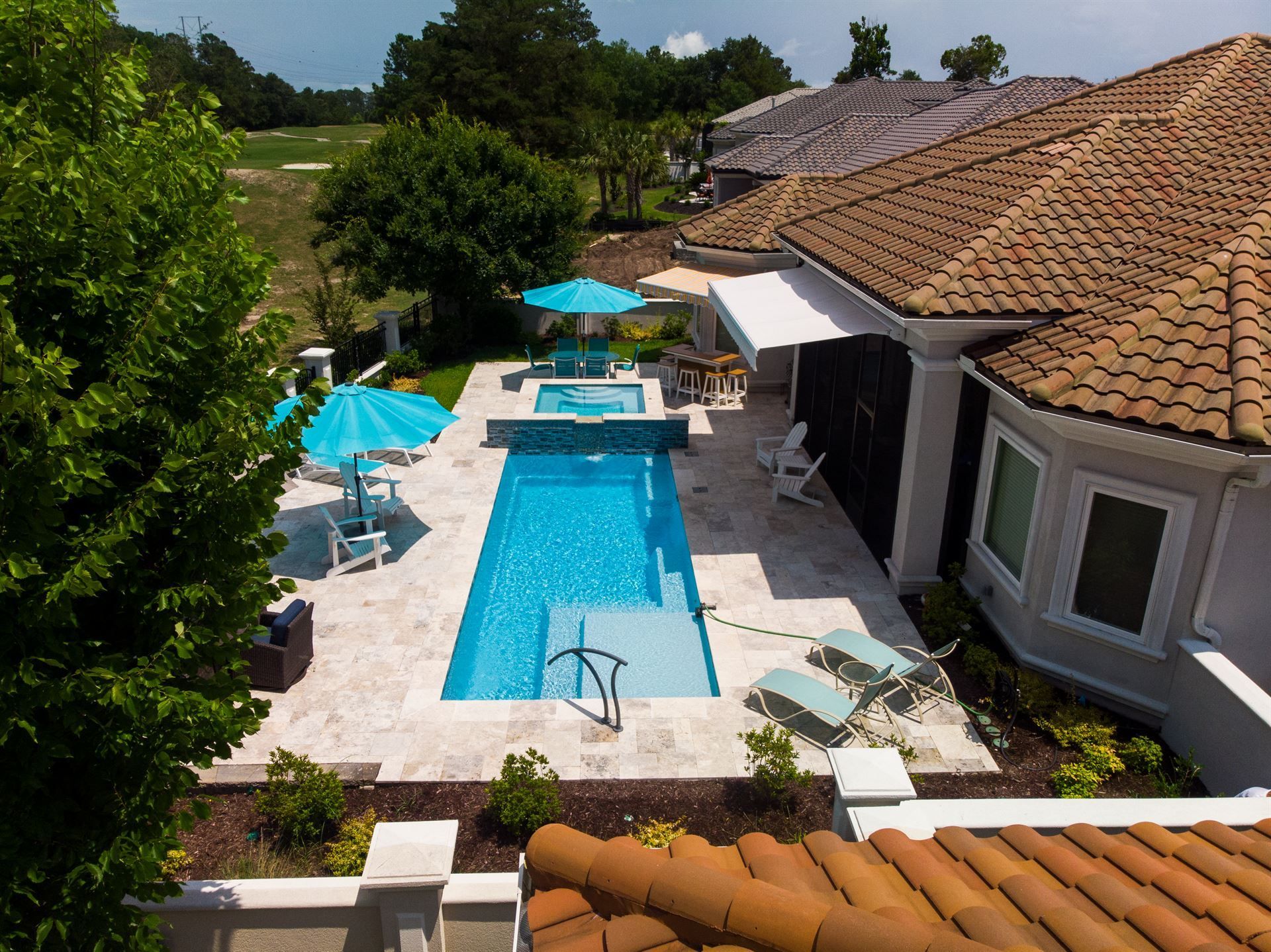 Aerial view of a backyard pool with blue umbrellas beside a house with a tiled roof.
