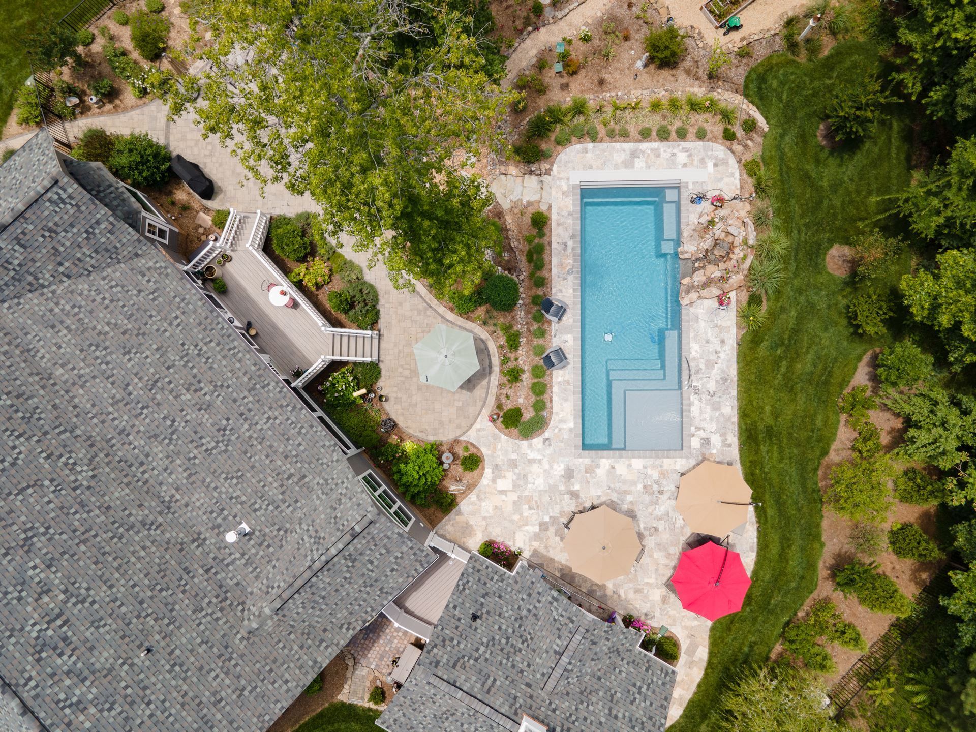 Aerial view of a backyard with a rectangular swimming pool, patio, and surrounding greenery