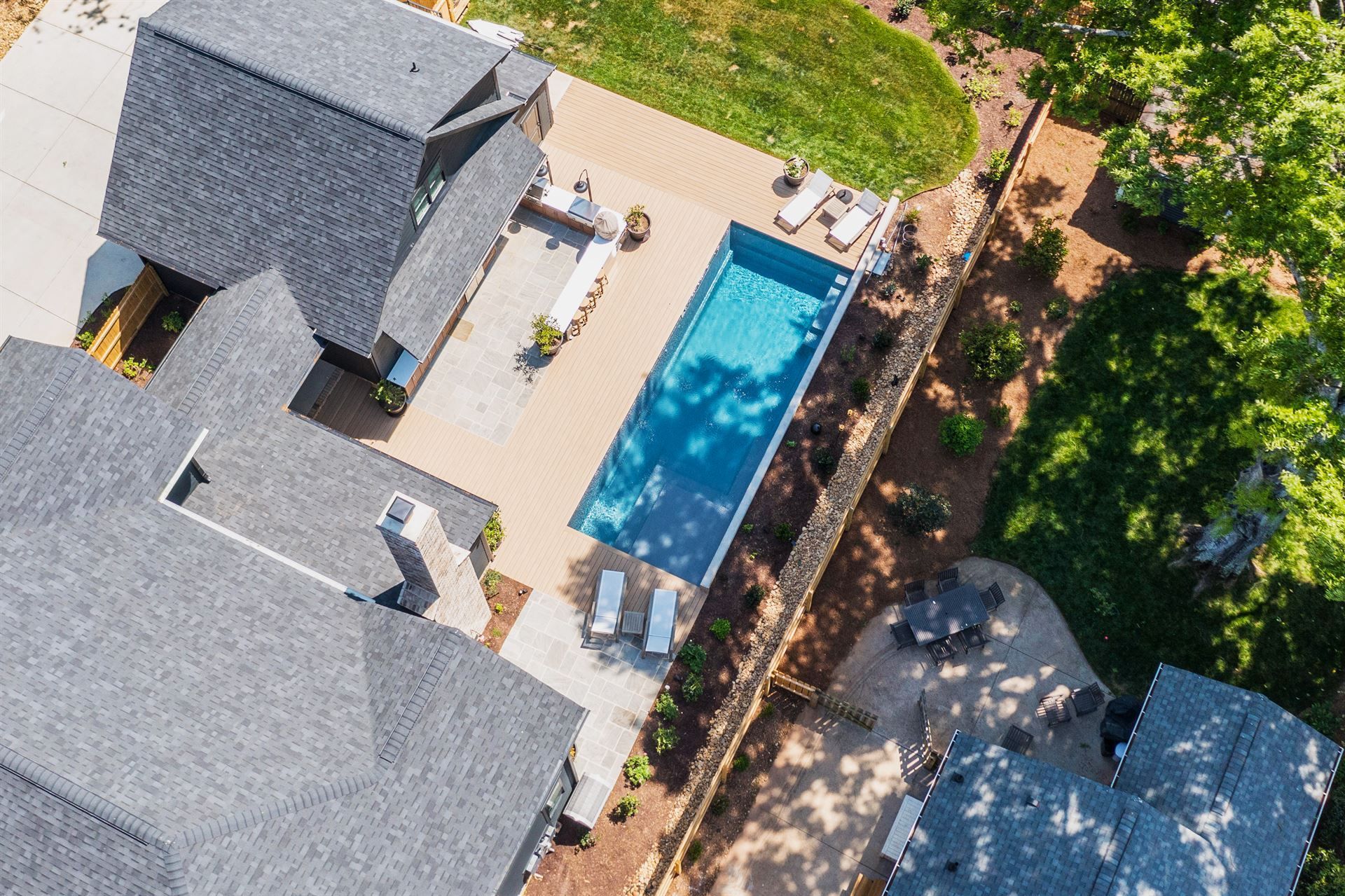 Aerial view of a backyard with a swimming pool, patio furniture, and surrounding trees next to a house