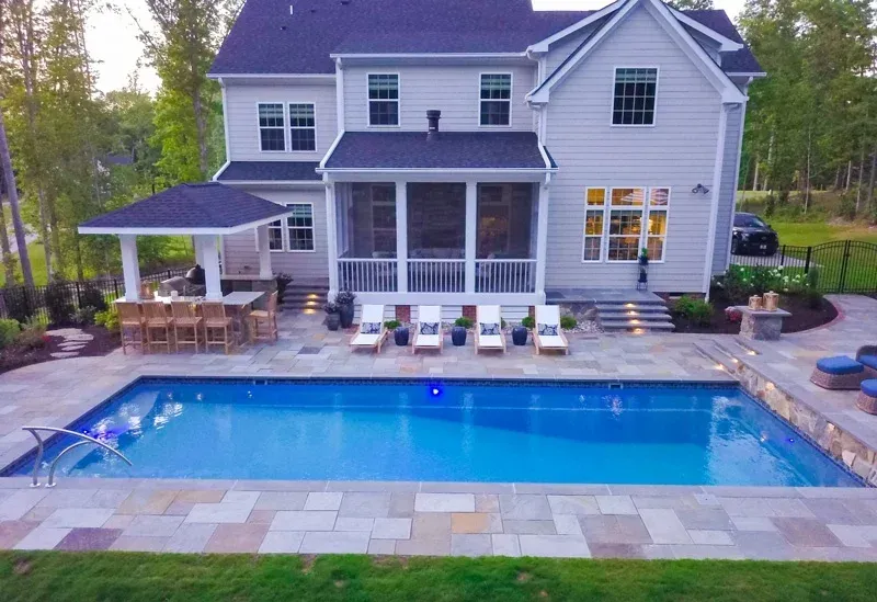 Backyard with a large blue swimming pool, patio lounge chairs, and a two-story house with a covered porch