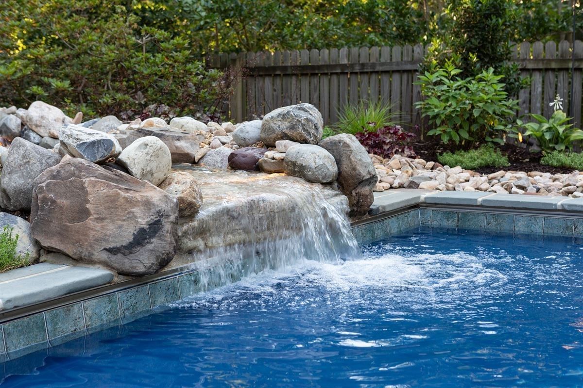 Backyard pool waterfall spilling over rocks into a blue swimming pool