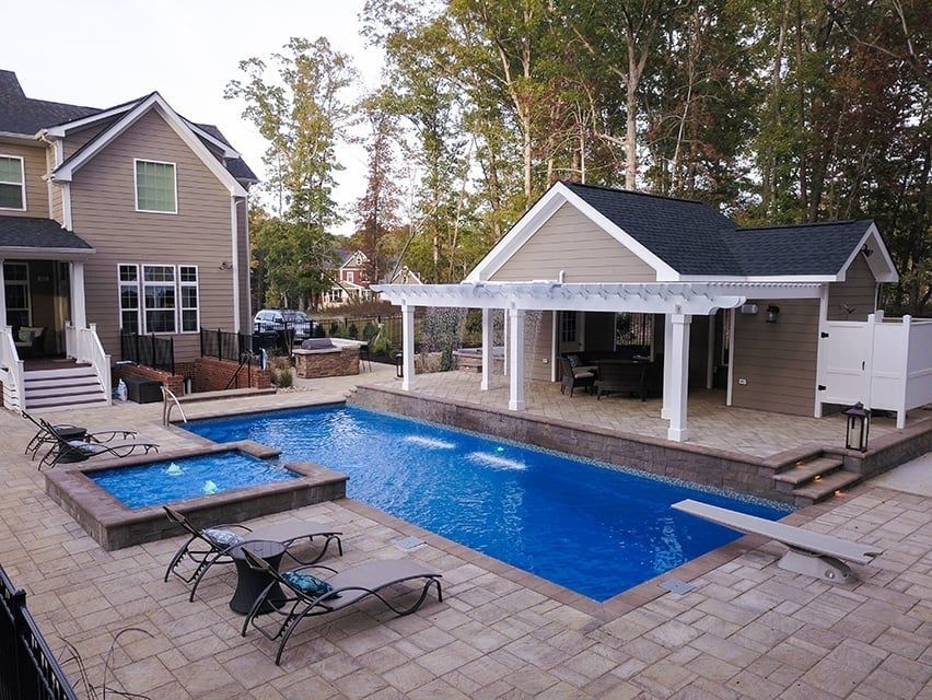 Backyard with rectangular blue pool, hot tub, lounge chairs, and a covered patio beside a house