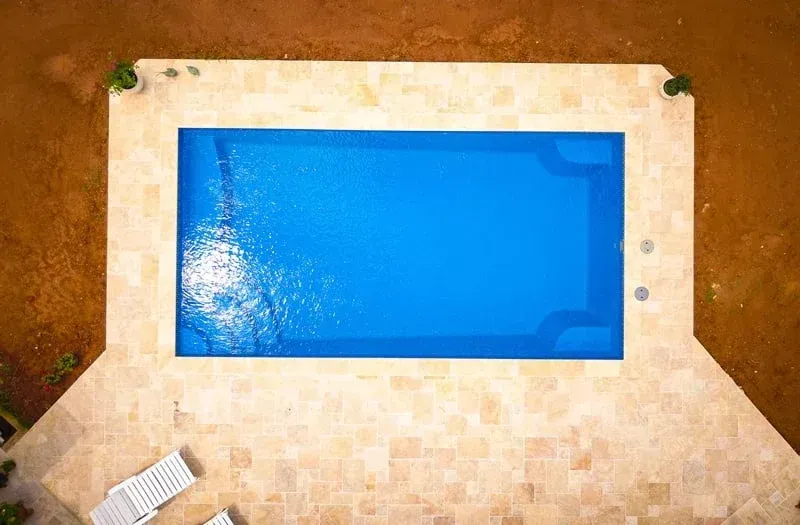 Blue swimming pool surrounded by tan stone patio, viewed from above