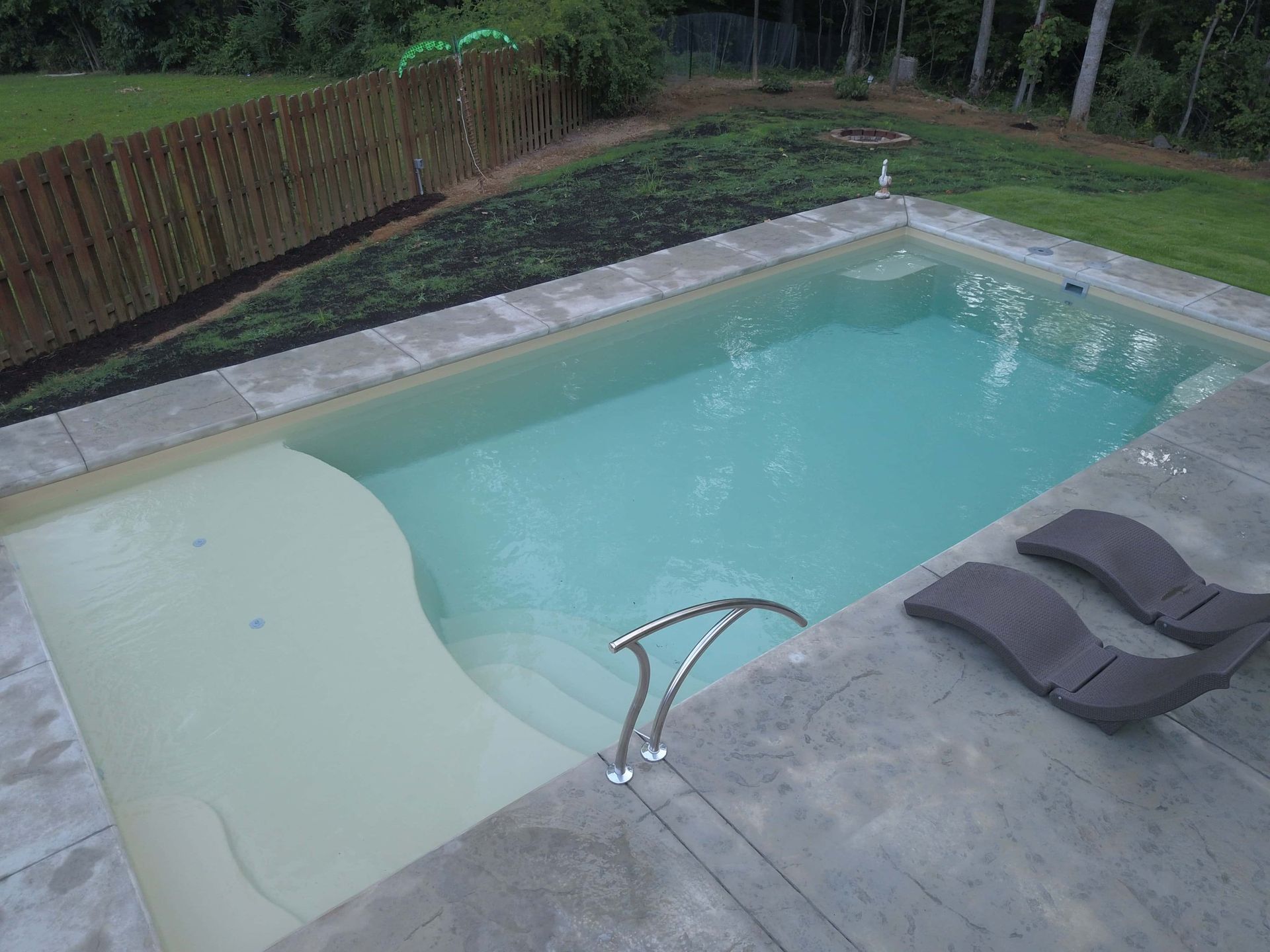 Backyard swimming pool with a shallow tanning ledge and two lounge chairs on the deck