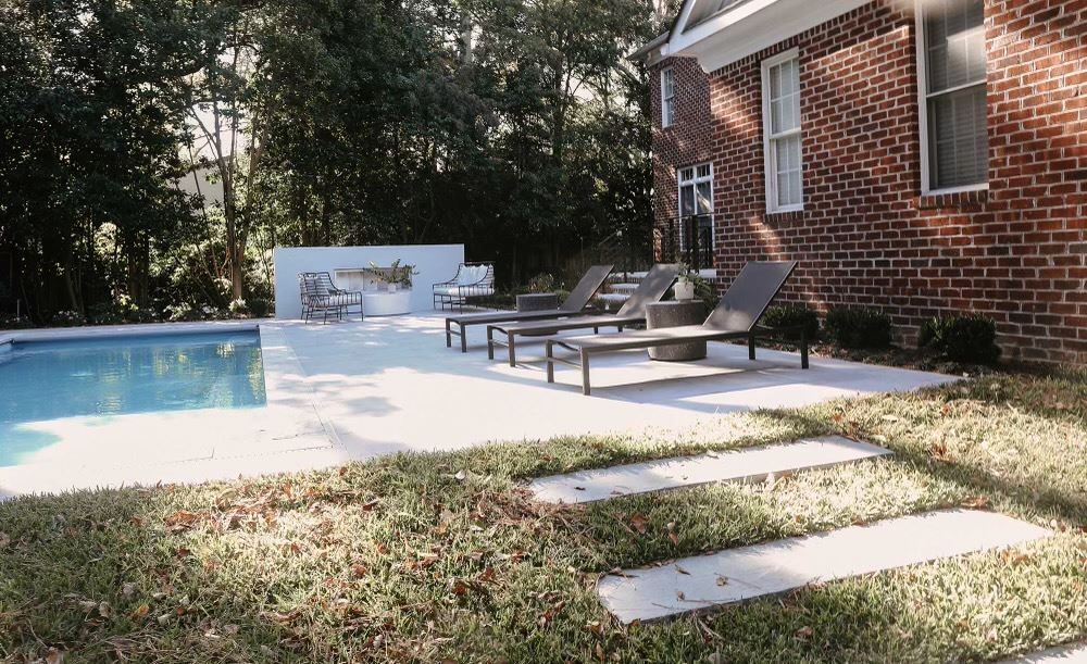 Backyard pool beside a brick house, with lounge chairs and stepping stones on a grassy lawn.