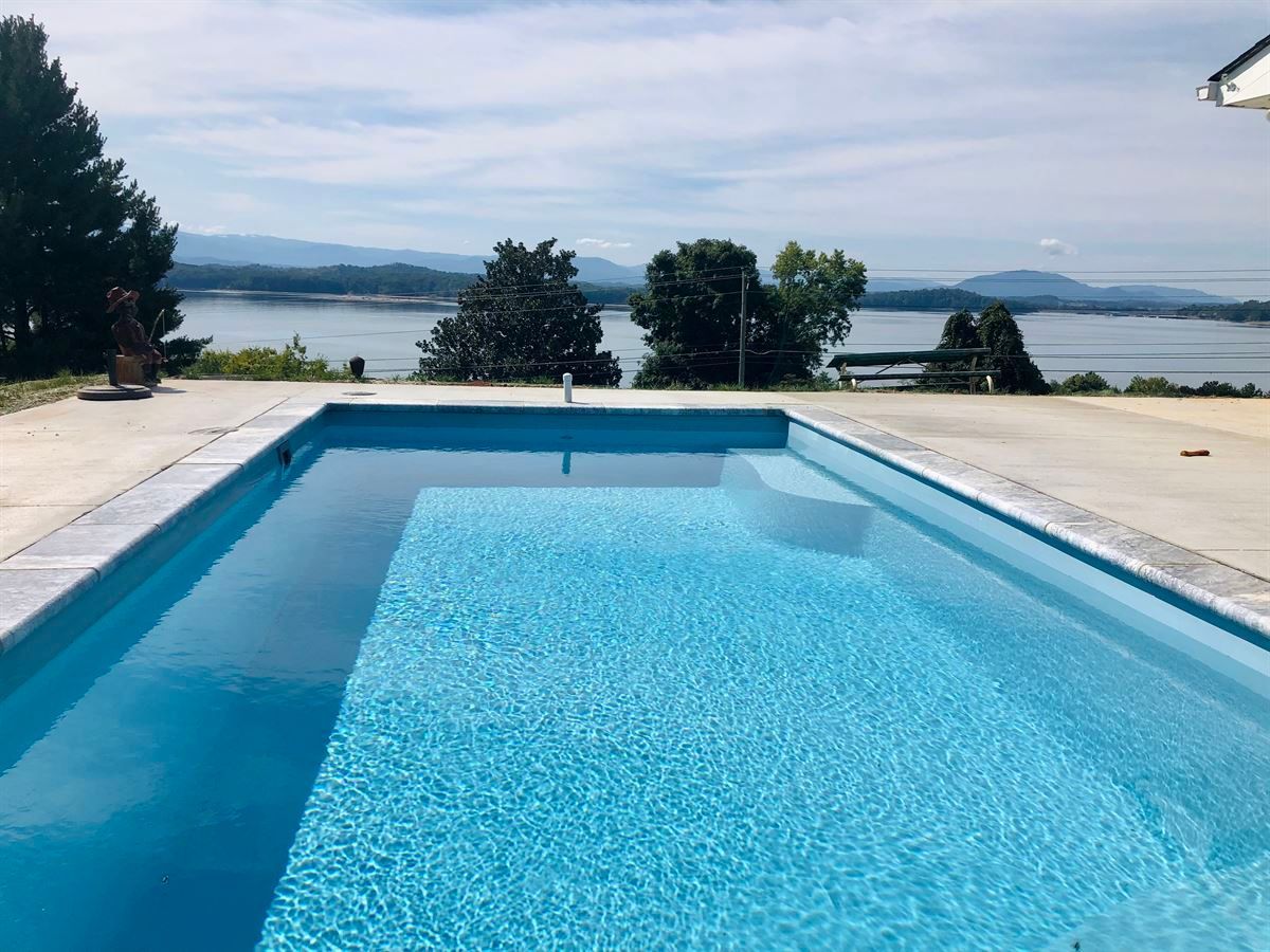 Blue swimming pool overlooking a calm lake and distant hills on a sunny day