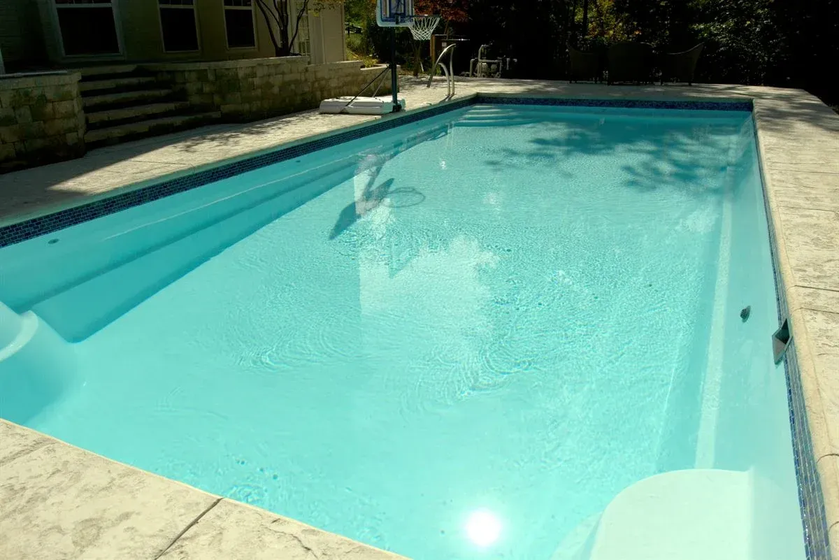 Sunlit backyard swimming pool with clear blue water and stone deck