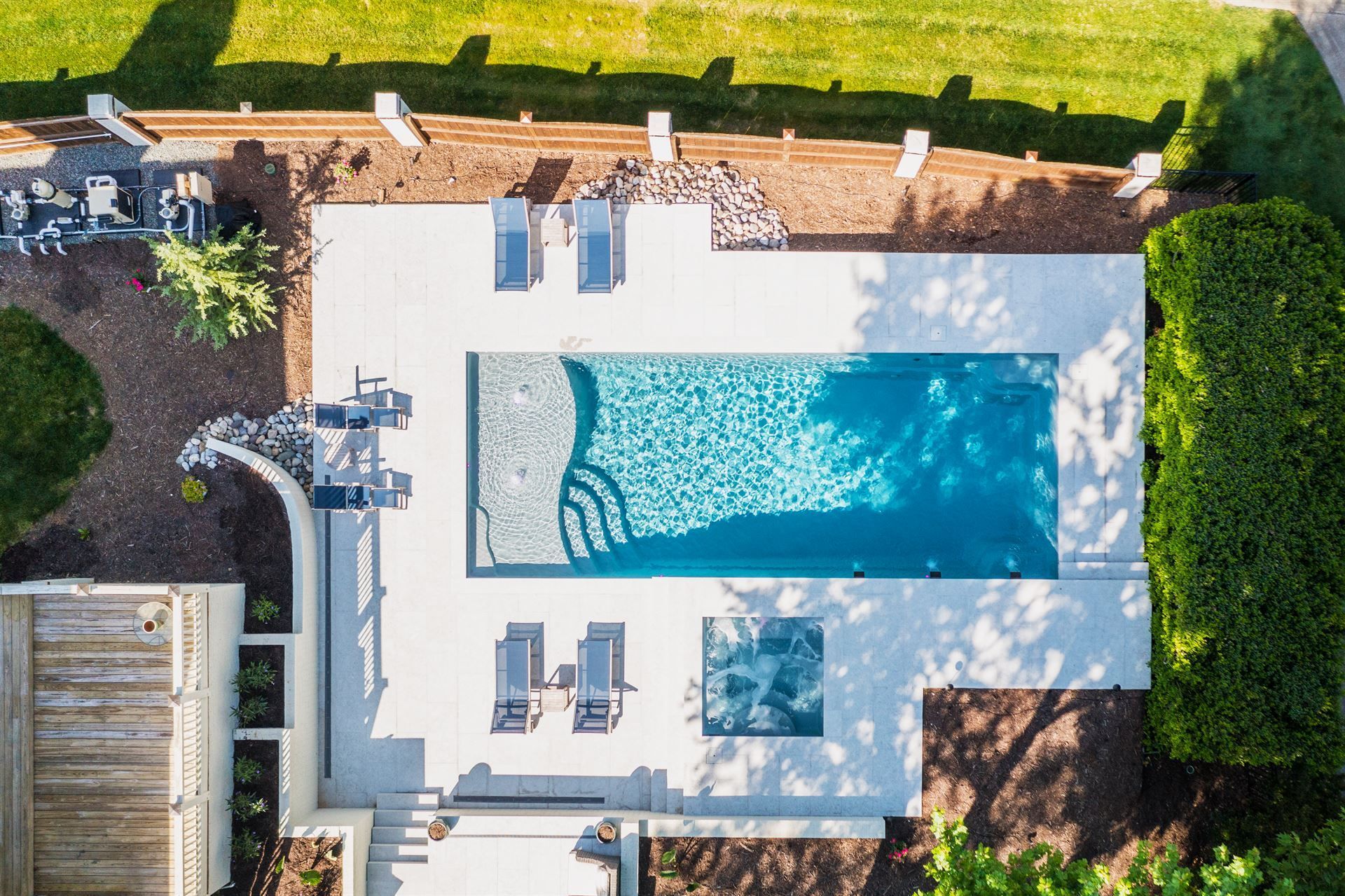 Aerial view of a backyard pool with white patio, two lounge chairs, and surrounding hedges and lawn