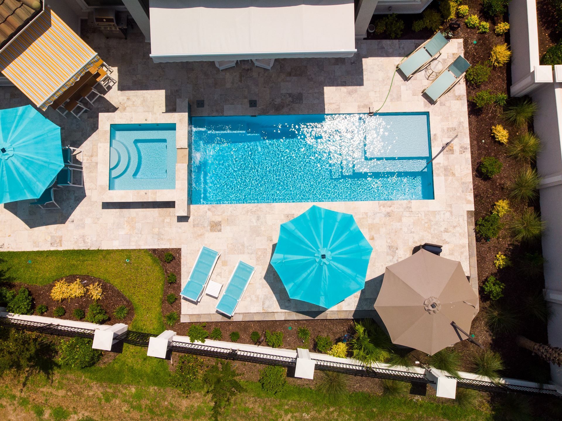 Aerial view of a backyard with a long pool, hot tub, lounge chairs, and patio umbrellas