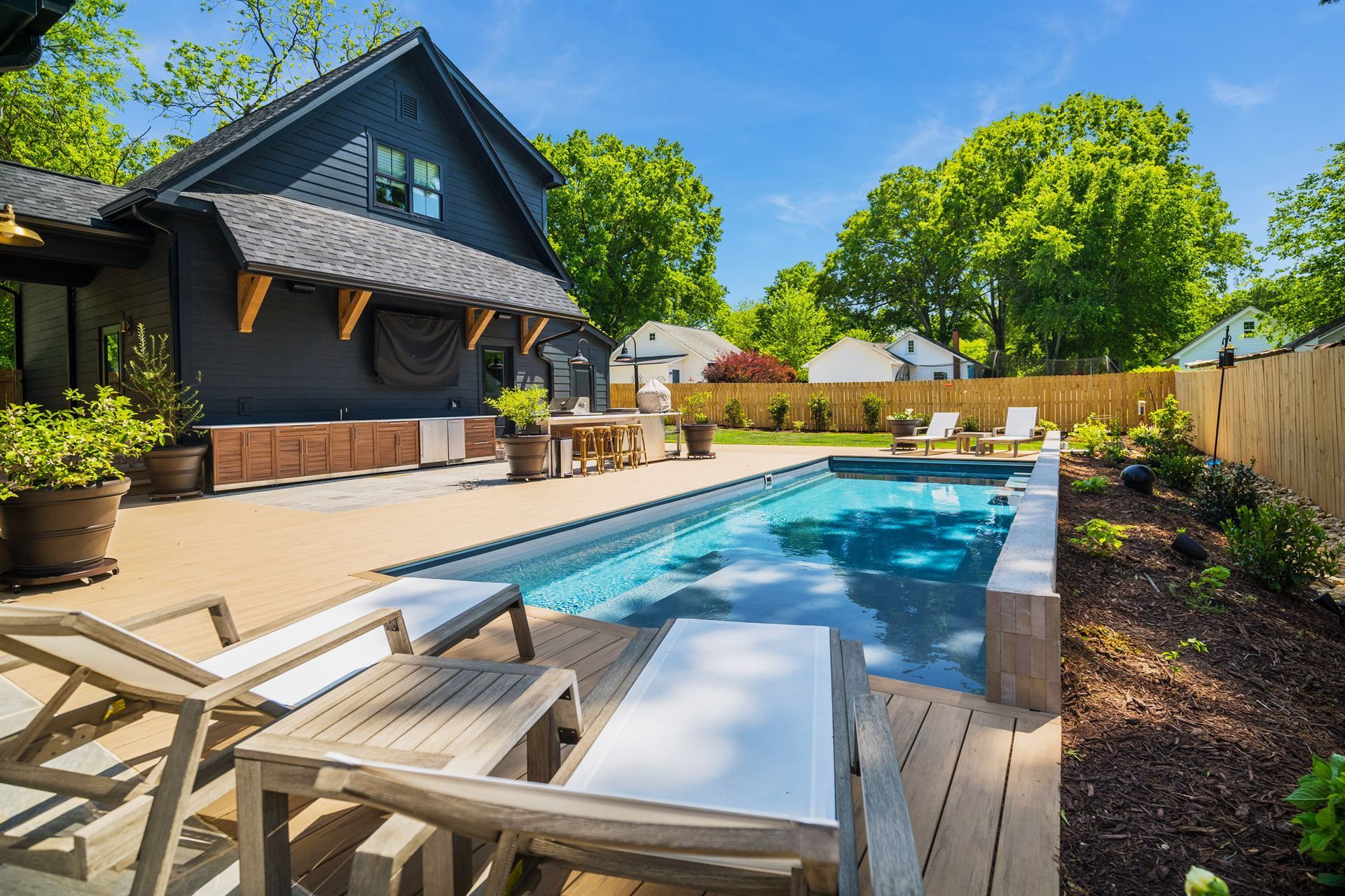 Backyard pool with lounge chairs beside a modern house and wooden fence under bright sun