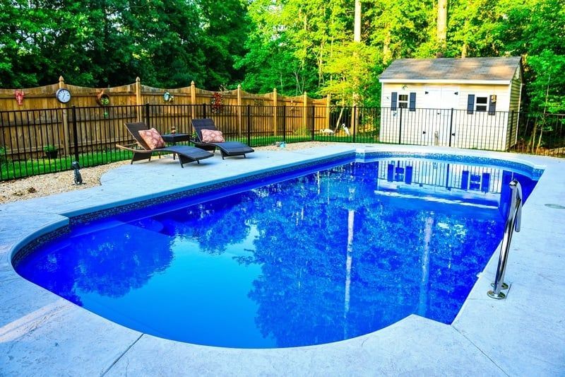 Backyard in-ground pool with blue water, lounge chairs, and a small shed behind a wooden fence