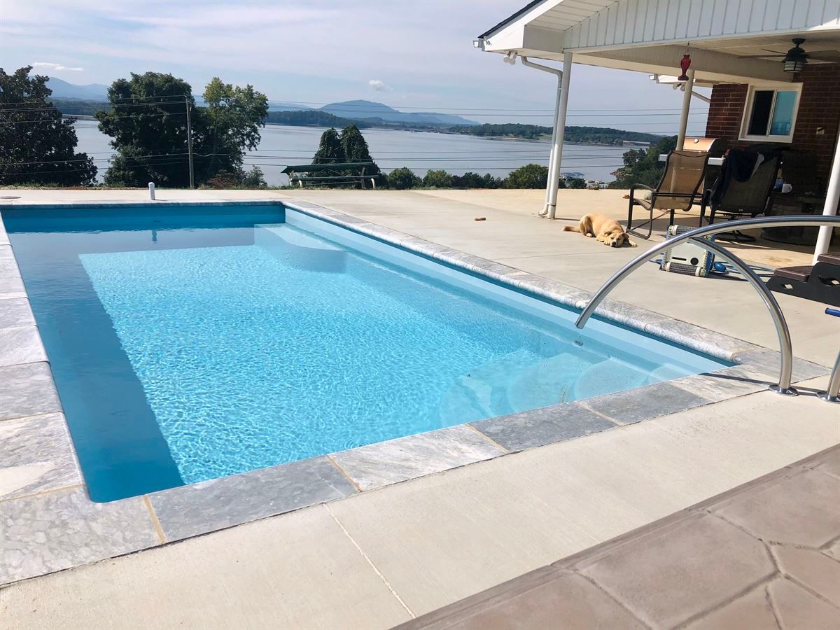 Infinity pool overlooking a calm lake and trees under a covered patio