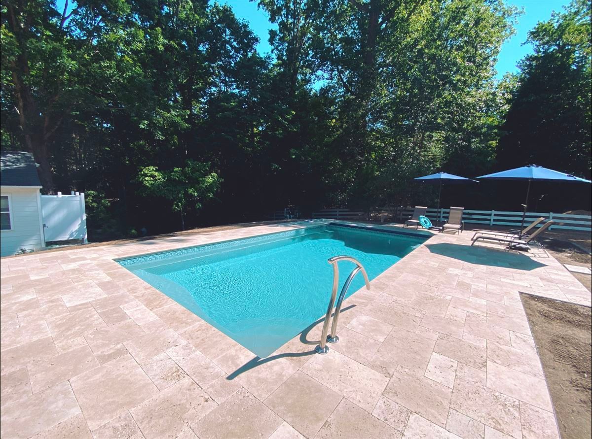 Backyard swimming pool with turquoise water, stone deck, trees, and a shaded lounge area