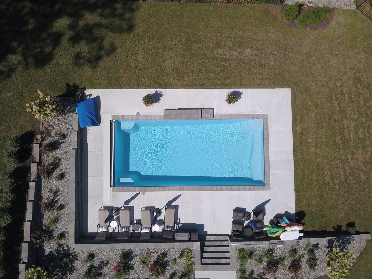 Aerial view of a backyard with a rectangular blue pool, lounge chairs, and patio seating on a white deck.