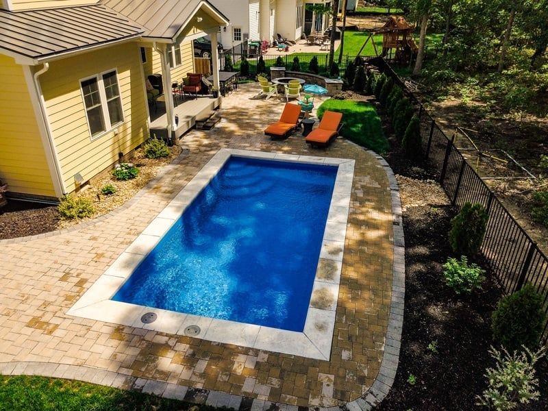 Backyard pool beside a yellow house, with lounge chairs and a paved patio.