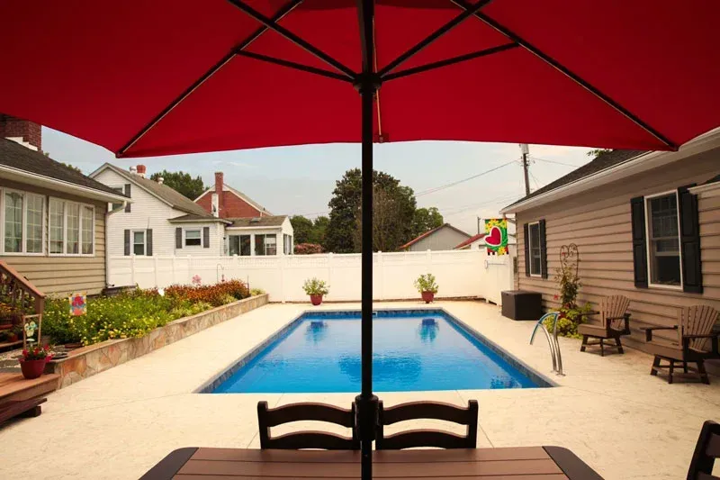 Backyard patio with red umbrella overlooking a small swimming pool and white fence