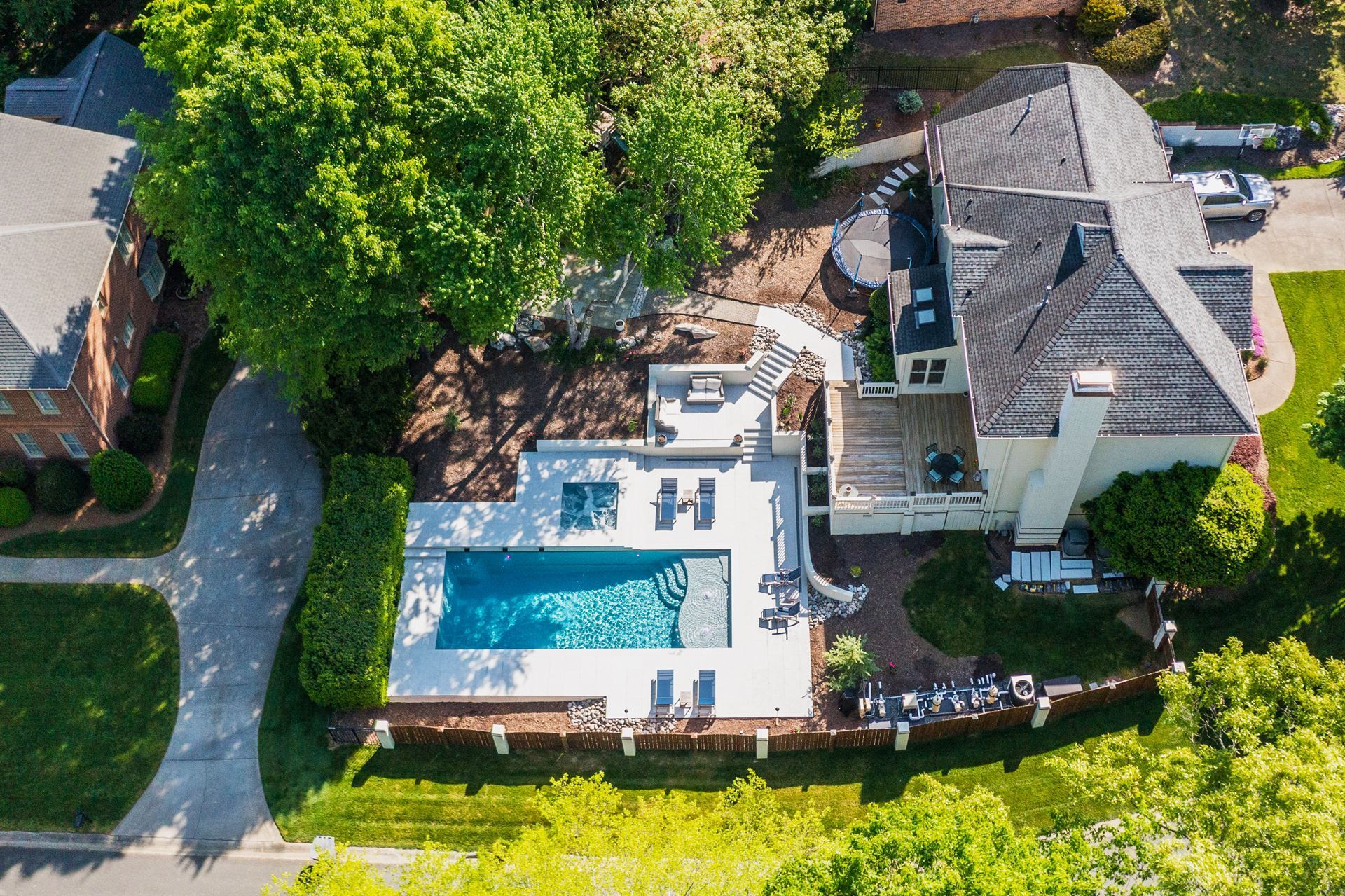 Aerial view of a house with a large swimming pool, patio, and trees in a landscaped yard