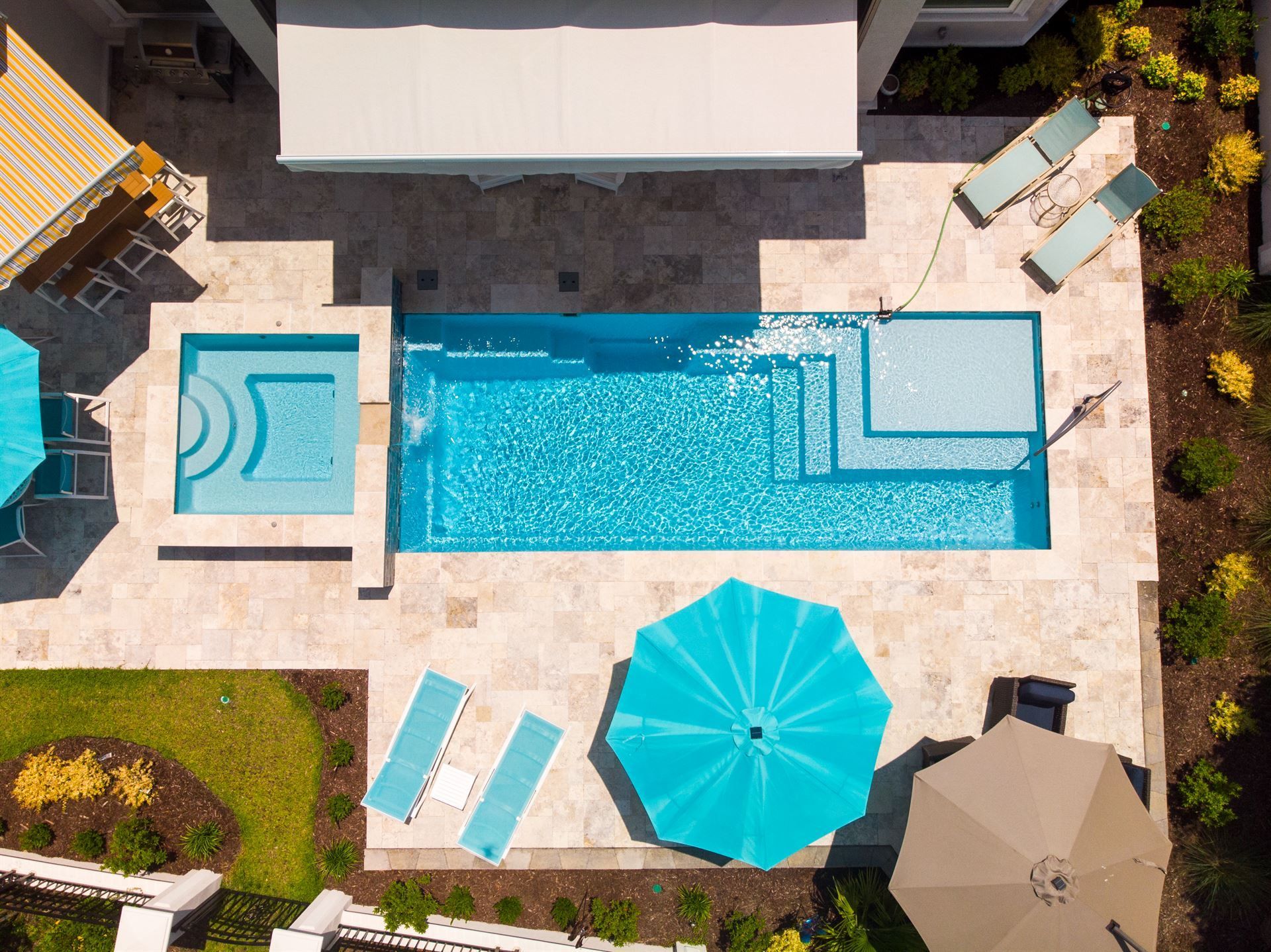 Aerial view of a backyard pool with turquoise water, lounge chairs, and umbrellas on a stone patio
