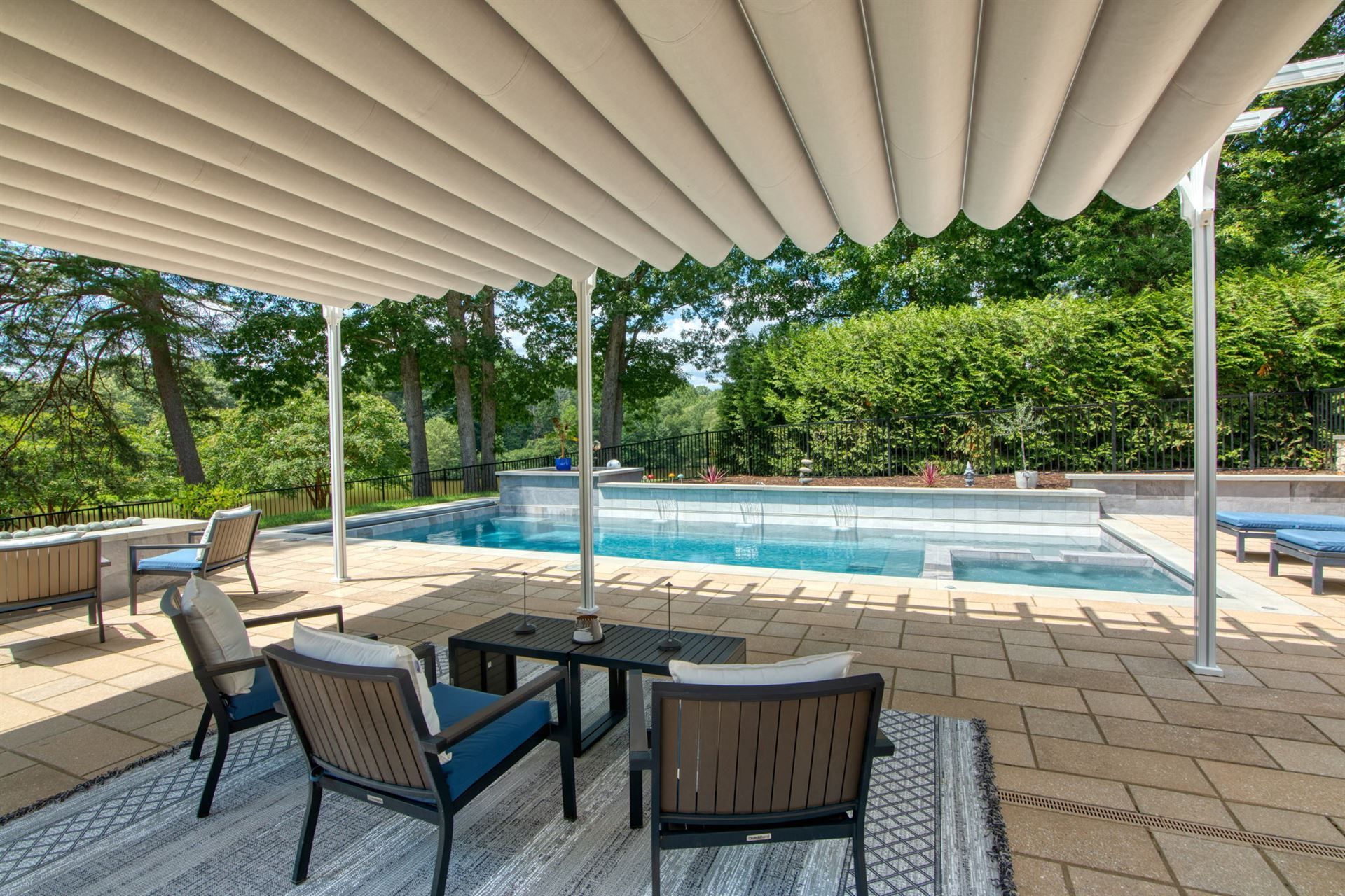 Covered patio with seating overlooking a swimming pool and green trees