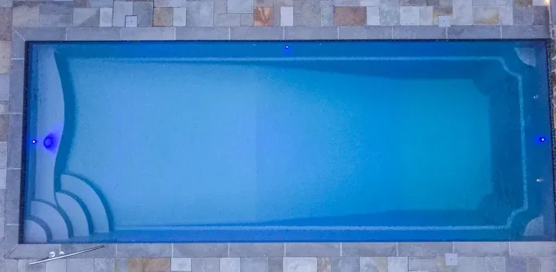 Top-down view of an empty blue swimming pool with a tiled border and steps in the corner