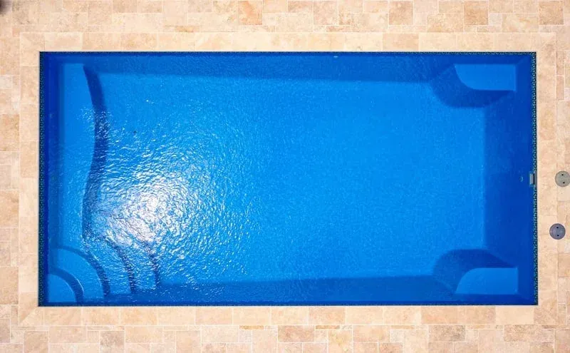 Blue rectangular swimming pool viewed from above, with water shimmering in sunlight.
