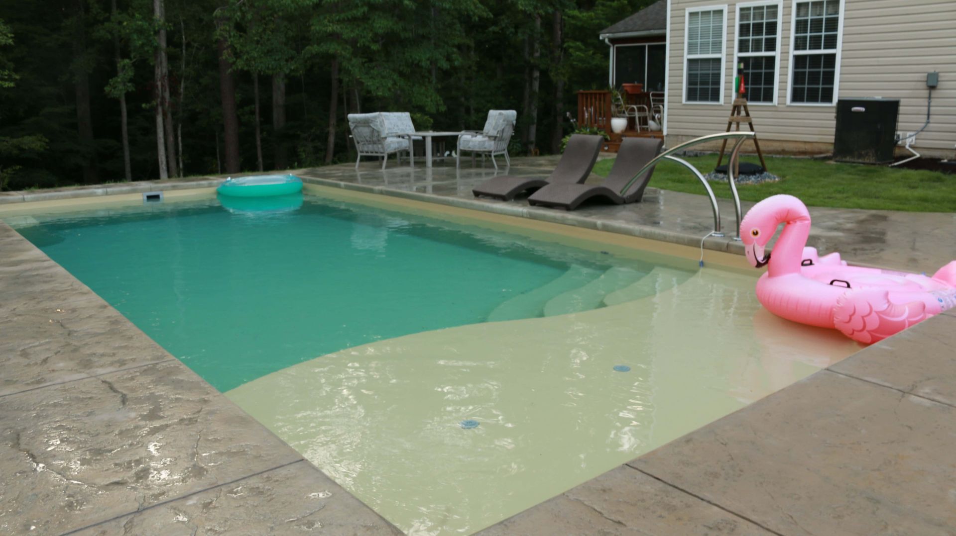 Backyard swimming pool with turquoise water, patio chairs, and a pink flamingo float near the deck