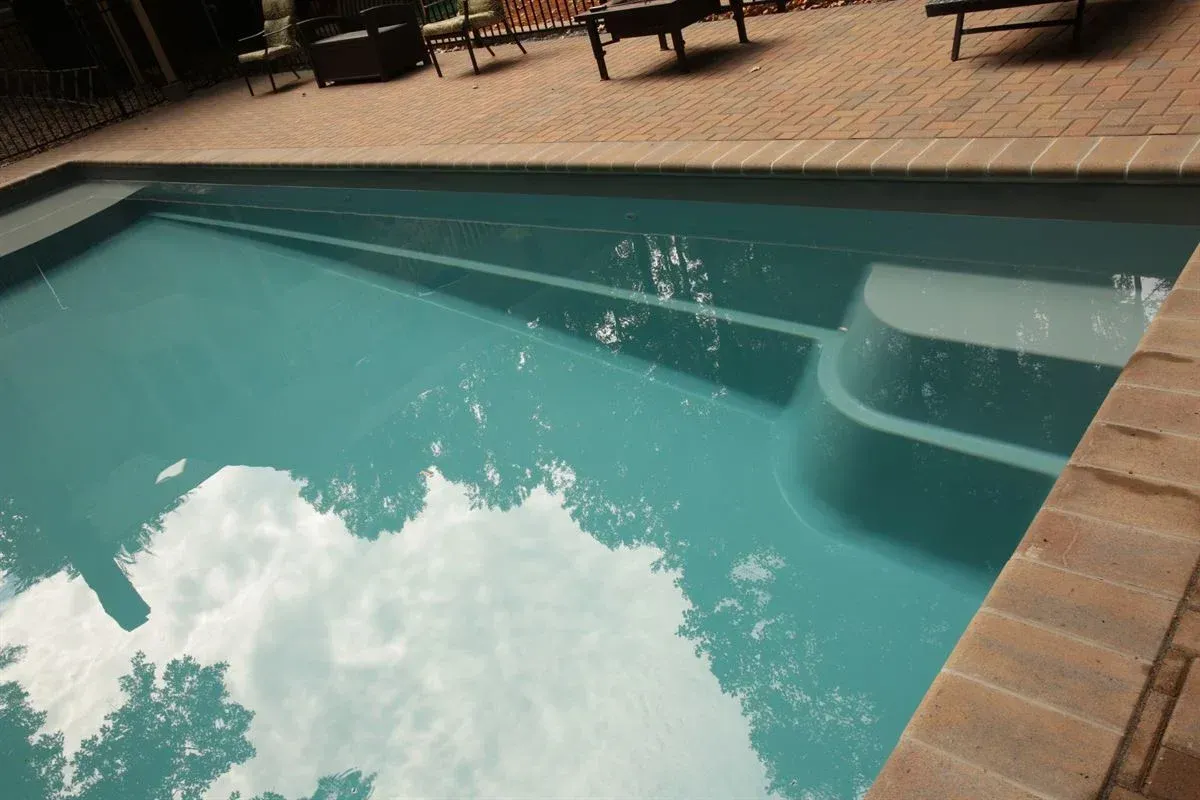 Outdoor swimming pool with turquoise water, brick deck, and underwater steps beside lounge chairs.