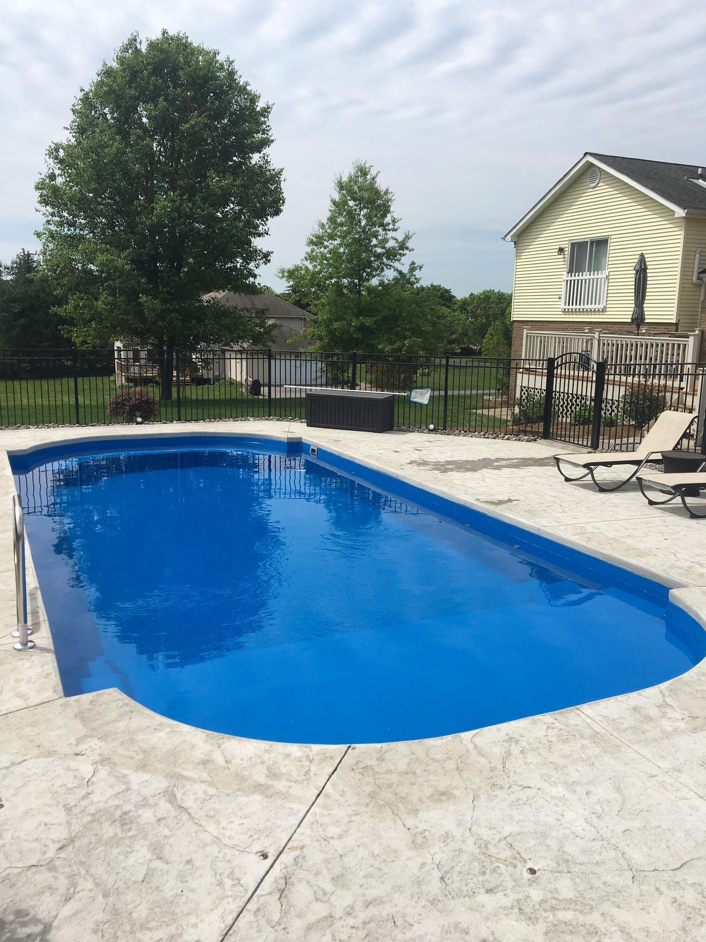 Backyard swimming pool with blue water, lounge chairs, trees, and a house nearby