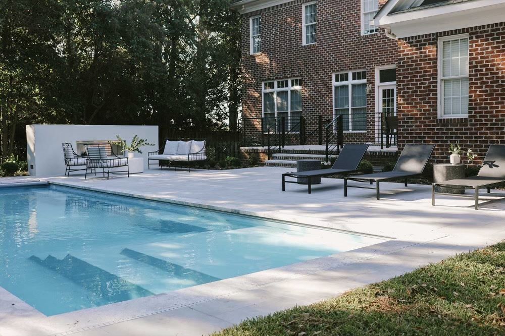 Backyard swimming pool beside a brick house with lounge chairs and patio seating
