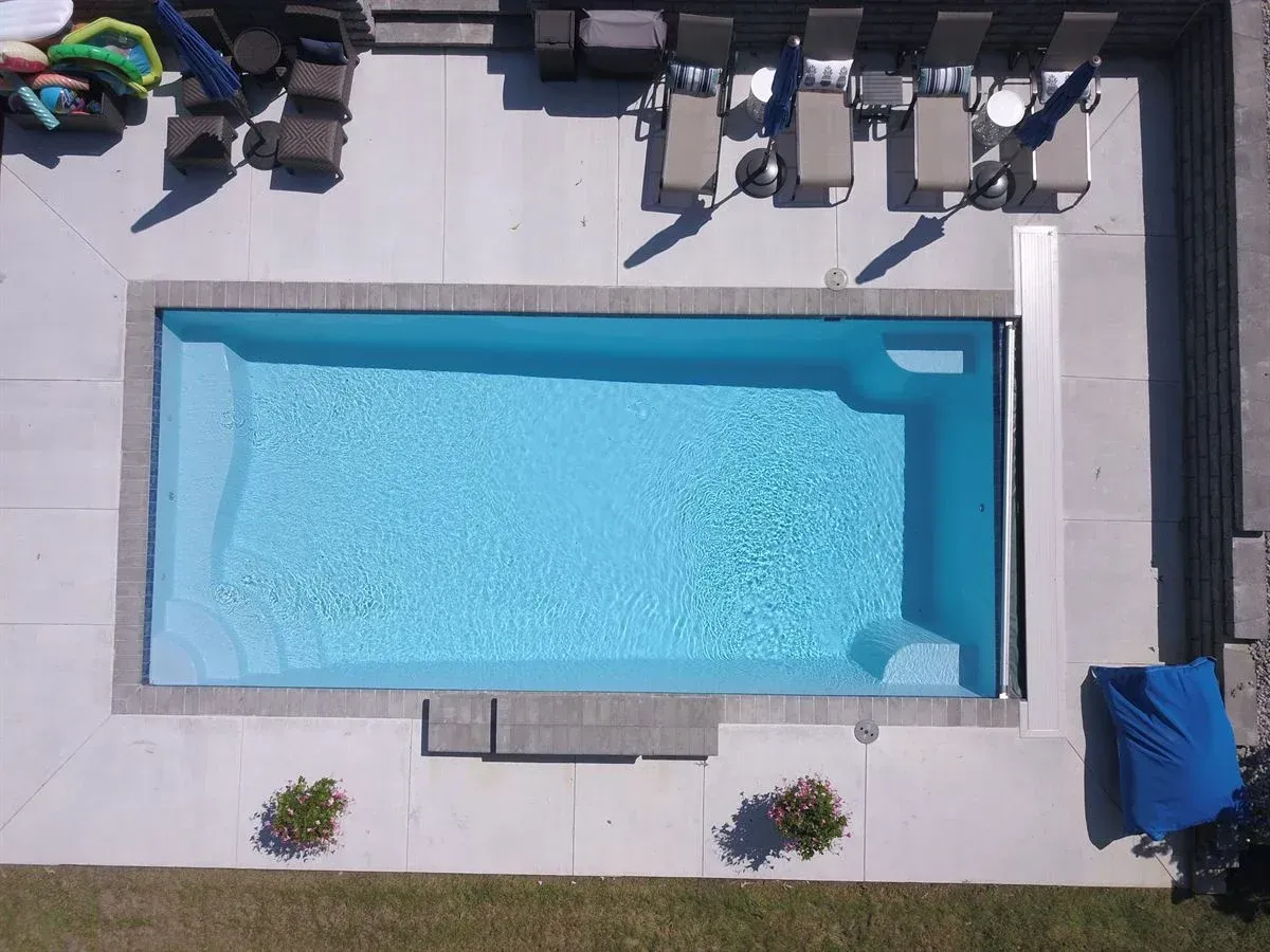 Aerial view of a rectangular swimming pool with lounge chairs and blue towels on a patio.